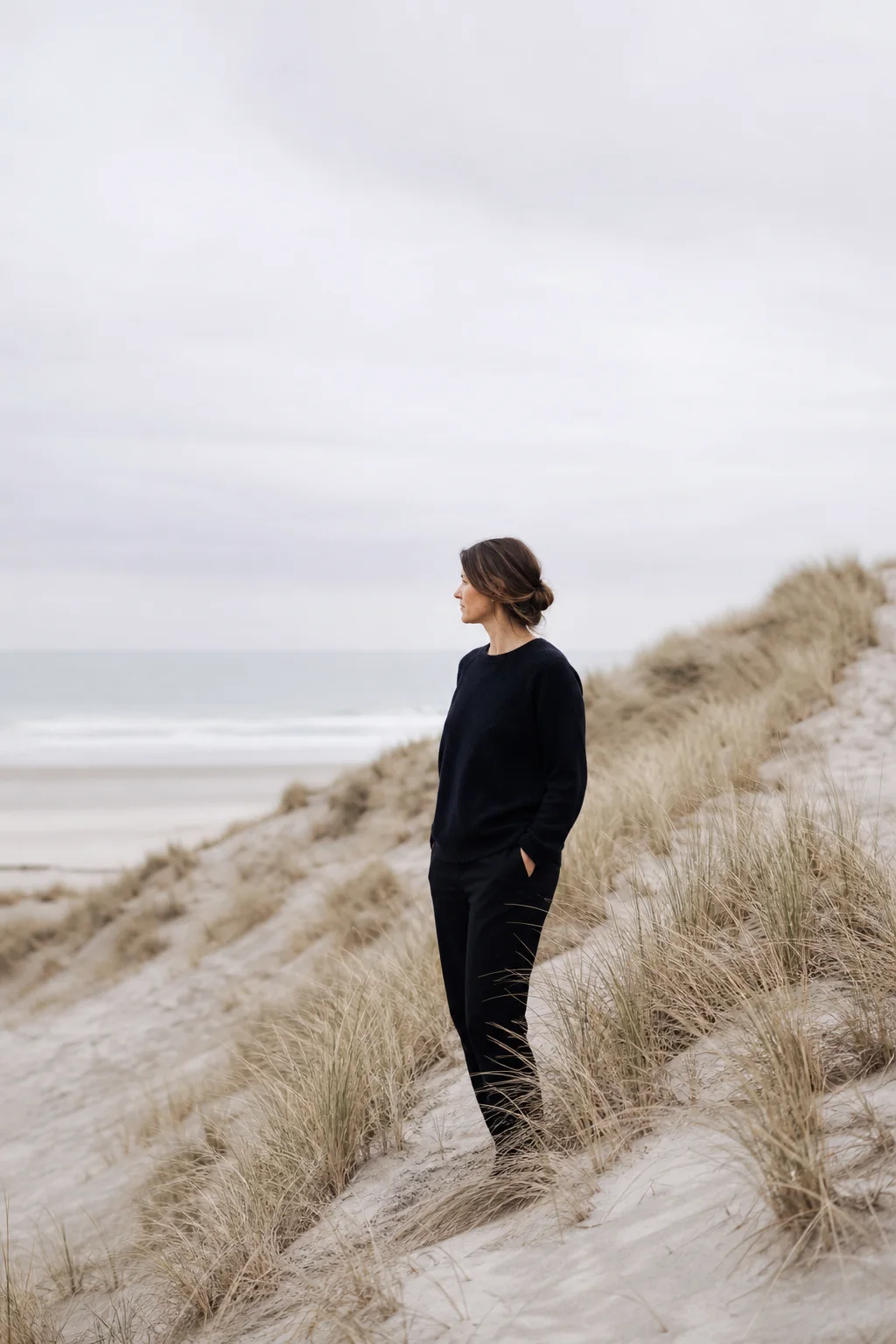 Portrait subject standing near wind-shaped dunes in clear coastal light.